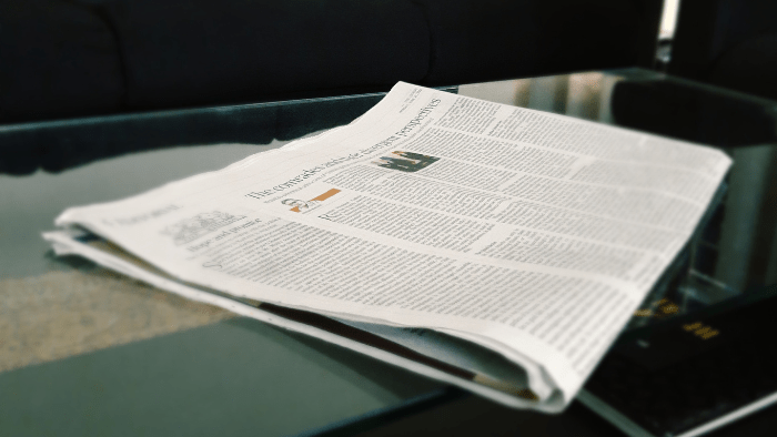 A folded newspaper on a glass table top