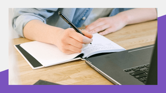 Person writing in a notebook in front of a laptop