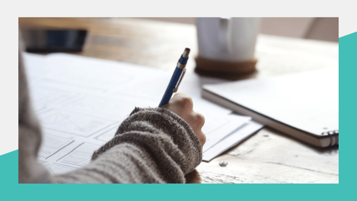 Person writing in notebook on tabletop with coffee mug nearby