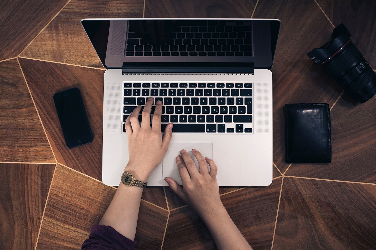 Overhead photo of a person typing a laptop with a cellphone and camera nearby