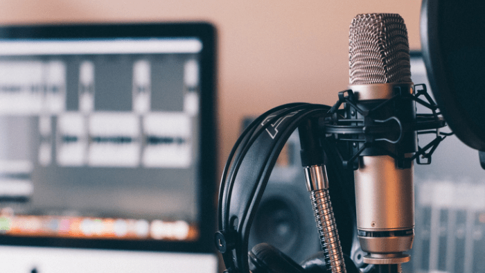 Podcast equipment, headphones hanging on a microphone with a computer monitor in the background