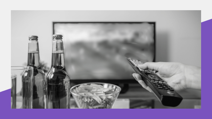 Person holding a remote while watching TV with beer and snacks